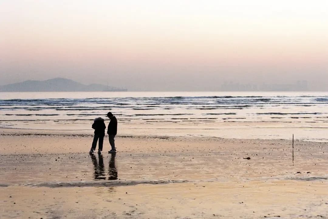 Two people standing on a wet sandy beach at sunset.