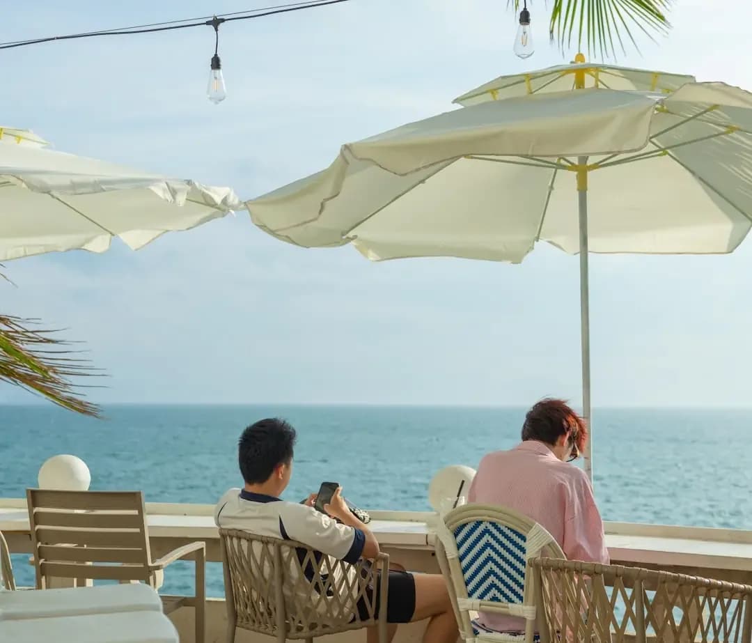 Two people relax at an outdoor cafe overlooking the ocean.
