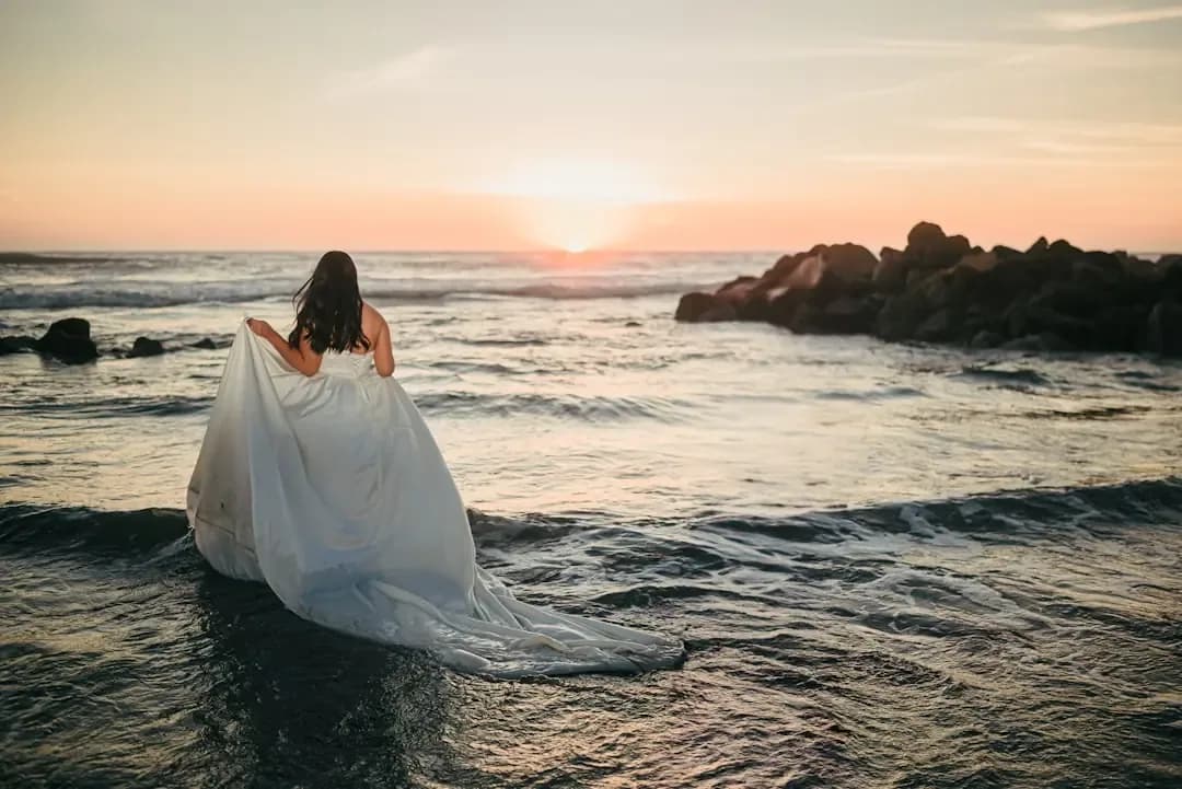 Woman in white dress walks into the ocean at sunset