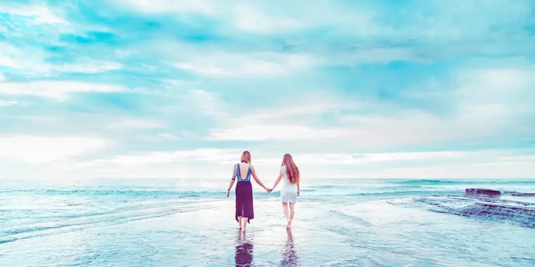 two women walking on shoreline holding hands
