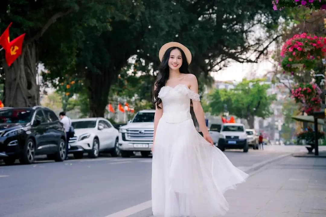 A woman in a white dress walks on a street.