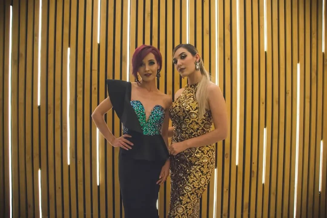 2 women in black and brown floral dresses standing beside brown wooden wall