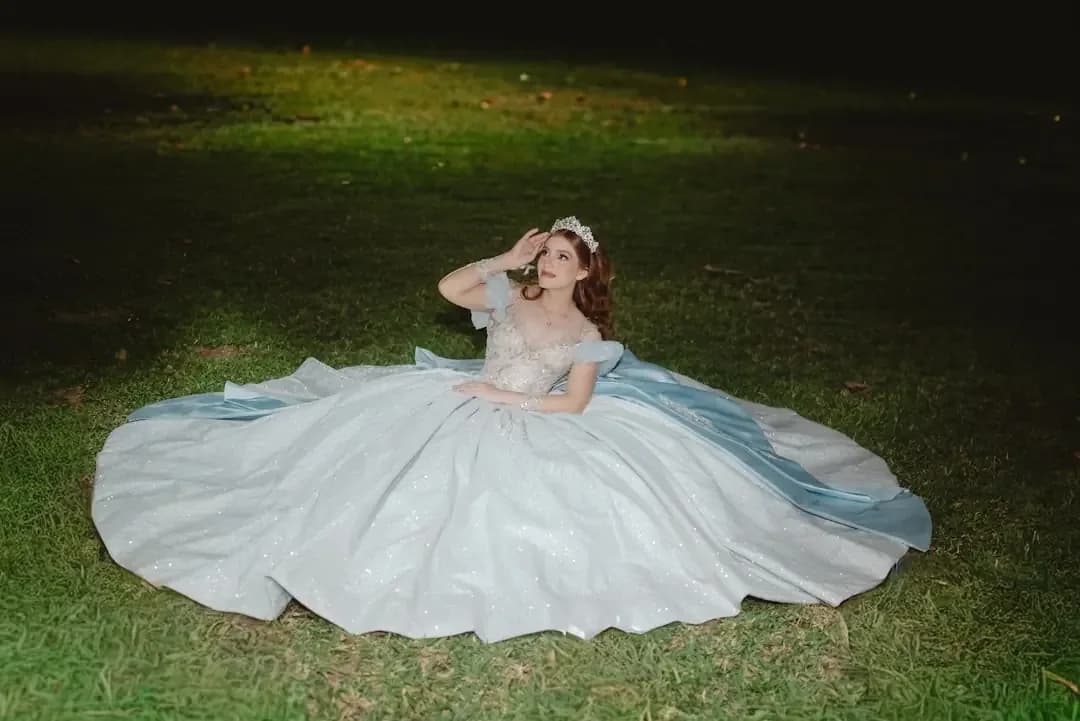 Woman in a flowing gown sits on grass at night.