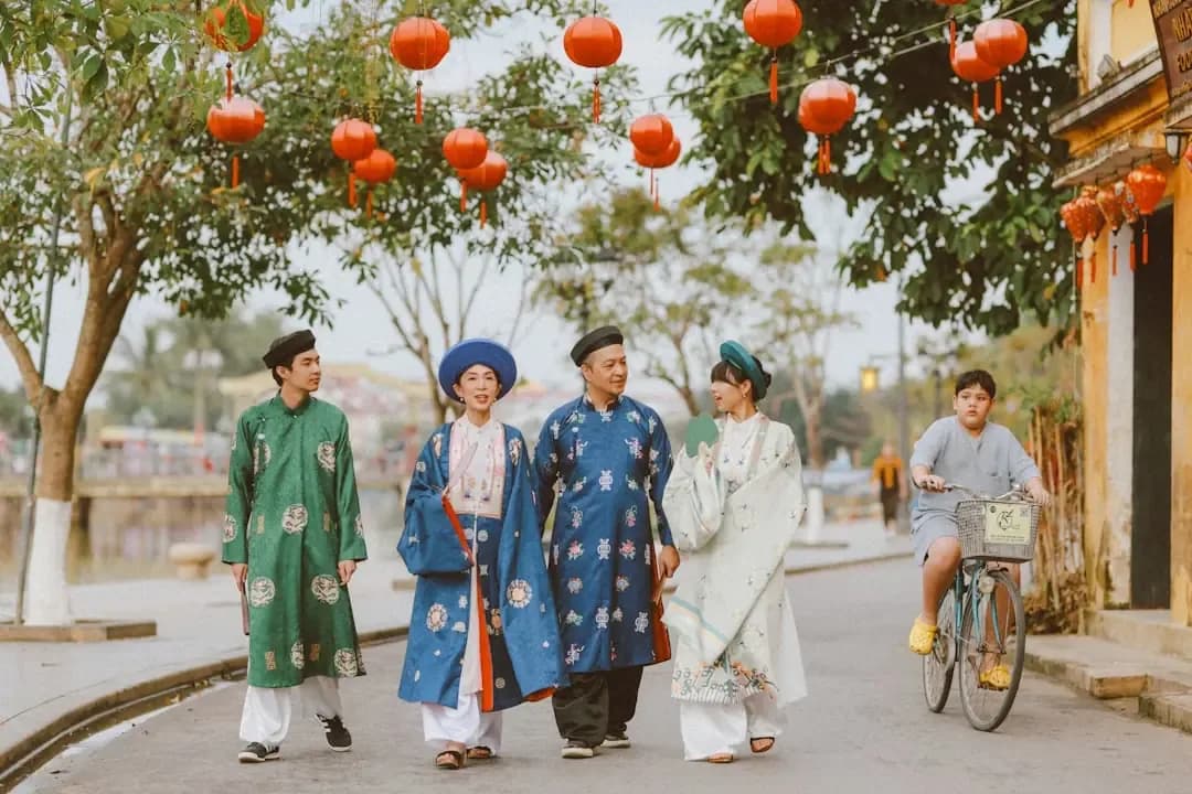 Four people in traditional vietnamese clothing walking on street.