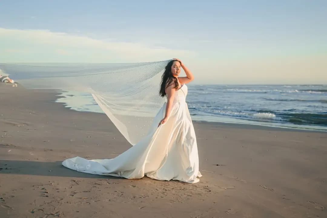 Bride in white dress on beach with veil blowing
