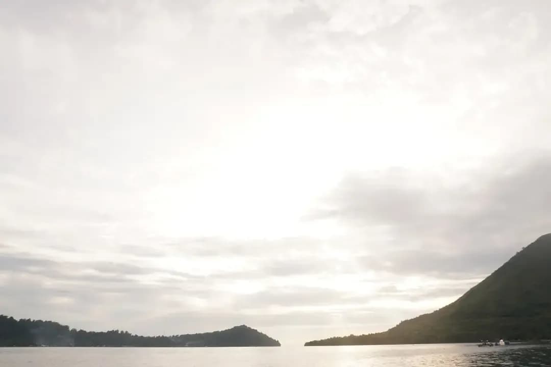 Calm ocean water with distant islands under cloudy sky.