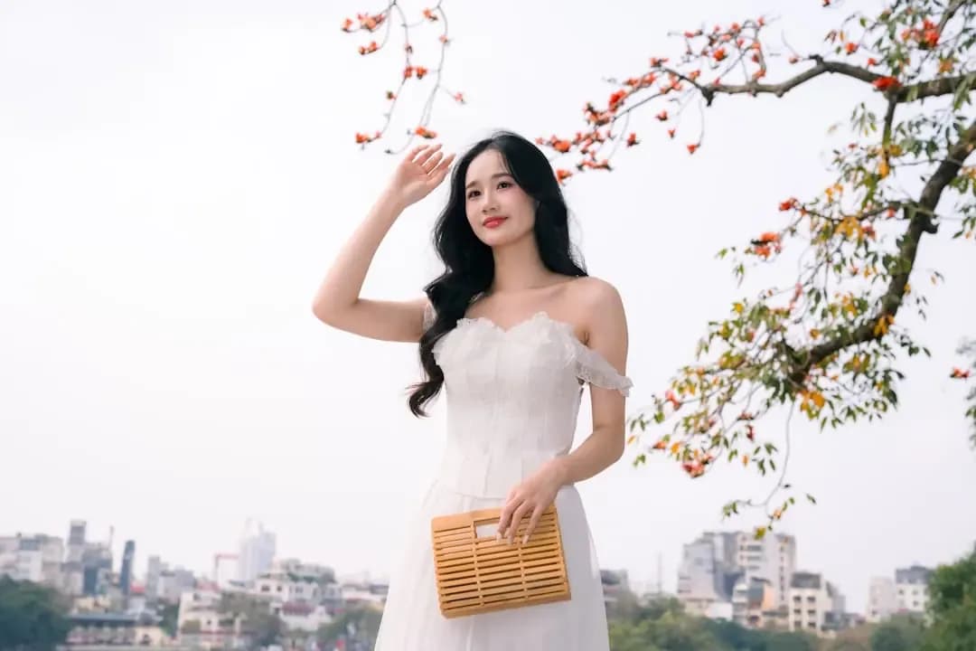 A woman in a white dress holds a woven bag.