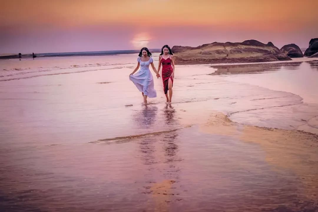 two women walking on the beach at sunset