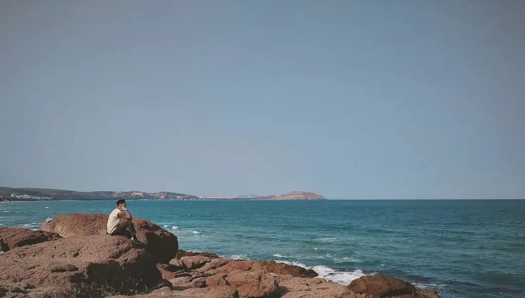 A person sits on rocks overlooking the ocean