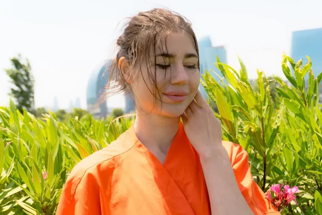 Young woman in orange shirt with plants and buildings